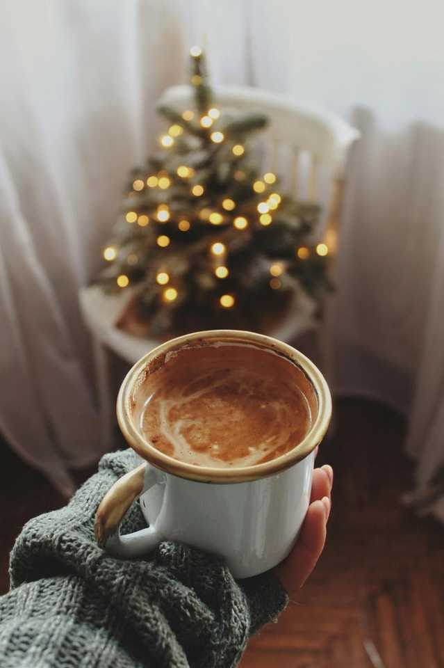 Honduran specialty coffee cup held in a cozy winter setting with Christmas lights – Fresh-roasted single-origin coffee from Raíces Coffee Roasters
